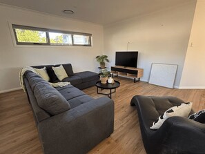 A modern living room with a sectional sofa, a smaller sofa, a coffee table, and a flat-screen TV on a wooden stand.