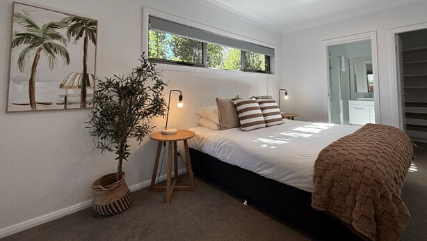 Ein Schlafzimmer mit einem Bett, Deckenventilator, Fenster, einer Pflanze und einem Wandbild.