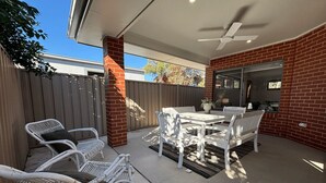 Eine Terrasse im Freien mit Tisch und Stühlen, einem Deckenventilator und einer Ziegelwand.