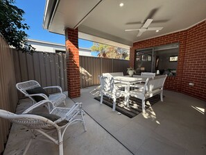 An outdoor patio with a table and chairs, a ceiling fan, and a brick wall.