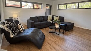 Ein modernes Wohnzimmer mit einer Eckcouch, einem geschwungenen schwarzen Ledersessel, einem kleinen runden Couchtisch und einer Stehlampe.