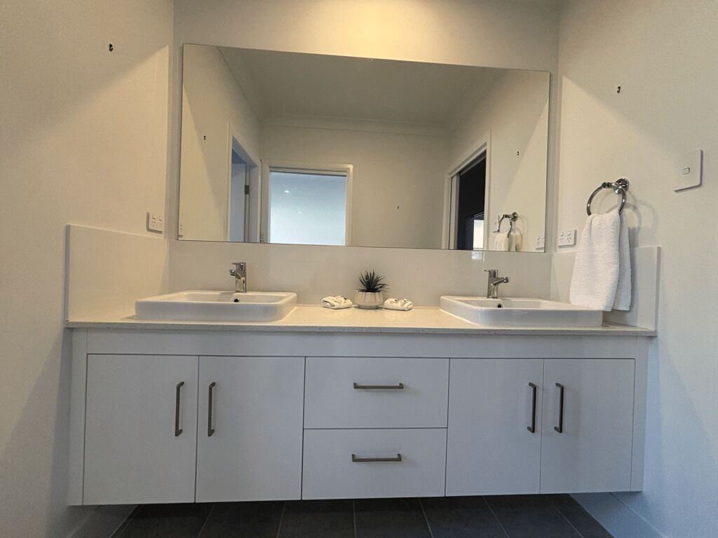 A modern bathroom with two sinks, a large mirror, and white cabinetry.