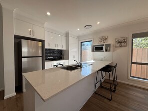 A modern kitchen with white cabinetry, stainless steel appliances, a large island with bar stools, and a window providing a view of the outdoors.