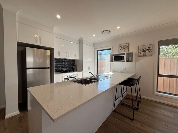 A modern kitchen with white cabinetry, stainless steel appliances, a large island with bar stools, and a window providing a view of the outdoors.