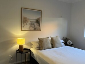 Une chambre à coucher avec un lit, une lampe de chevet, une table de chevet, une plante en pot et un tableau accroché au mur.