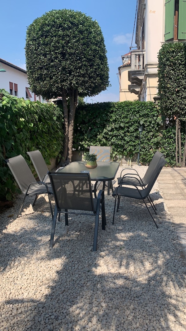 Un área de estar al aire libre con una mesa y sillas, rodeada de grava y follaje.