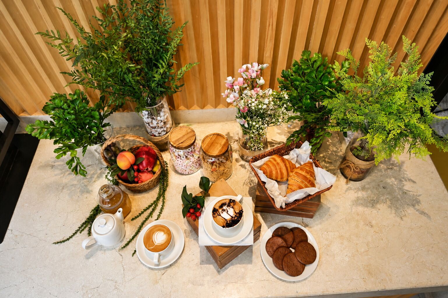 Une table dressée avec du café, des pâtisseries, des fruits et des plantes décoratives.