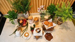 A table set with coffee, pastries, fruits, and decorative plants.