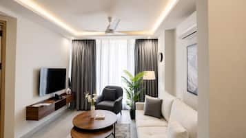 Een moderne woonkamer met een flatscreen televisie, een bank, een fauteuil, een salontafel en een potplant.