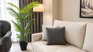 A living room with a sofa, a potted plant, a lamp, and a painting on the wall.