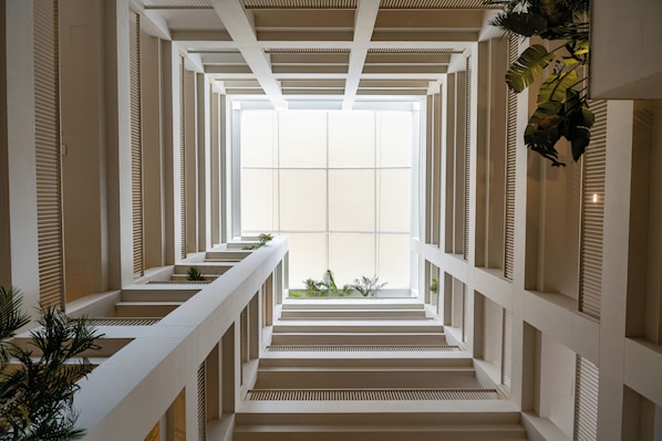 Un intérieur moderne avec un escalier central, des rampes blanches et une grande fenêtre en haut.