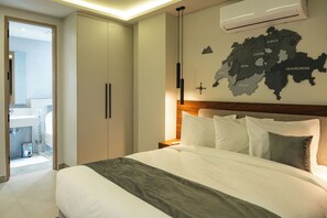 Une chambre d’hôtel moderne avec un grand lit, une tête de lit en bois, une carte géographique accrochée au mur et une salle de bain visible à travers une porte ouverte.