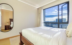 Ein Schlafzimmer mit großem Fenster, einem Bett, einem Spiegel und einem Nachttisch mit einer Vase.