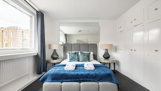 Habitación de hotel con cama, dos mesitas de noche, un espejo grande, armario y ventana con cortinas.