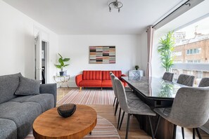 Ett modernt vardagsrum med en soffa, ett matbord med stolar, en röd soffa, en växt och en tavla på väggen.