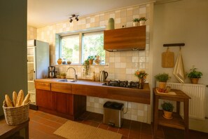 Eine Küche mit Holzausziehtisch, Spüle, einem Fenster mit Pflanzen, einer hängenden Pfannenträger und einer Heizung.