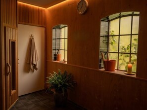 A hallway with wooden walls, a clock, a towel rack, a potted plant, and windows with plants. - Voorhuis with private sauna near Leeuwarden - sleeps 6 (Weidum)
