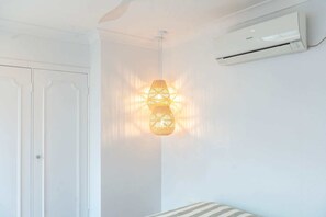 A room with white walls, a white door, a ceiling-mounted air conditioner, and a hanging light fixture. - Montipora Airlie Beach Oceanfront Apartment (Airlie Beach)