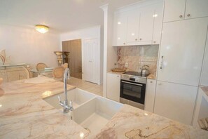 A modern kitchen with a marble countertop, built-in oven, and white cabinetry. - Montipora Airlie Beach Oceanfront Apartment (Airlie Beach)