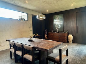 Uma área de refeições com mesa e cadeiras de madeira, luminária pendente, cômoda e um espelho grande.