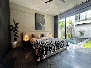 Quarto moderno com cama grande, ventilador de teto, luminária na parede e vista para uma piscina.