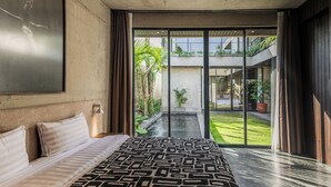 A modern bedroom with a large bed, a view of a courtyard, and a balcony with plants. - Seseh House by Alfred in Bali (Cemagi)