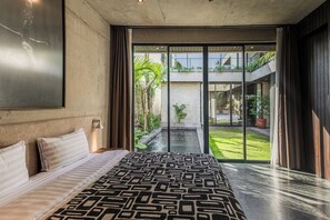 Ein modernes Schlafzimmer mit einem großen Bett, Blick auf einen Innenhof und einem Balkon mit Pflanzen.