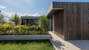 A modern building with a wooden facade, a concrete section, and a well-maintained garden with various plants. - Seseh House by Alfred in Bali (Cemagi)