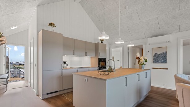 Et moderne køkken med en stor ø, hvide skabe og hængende lamper.