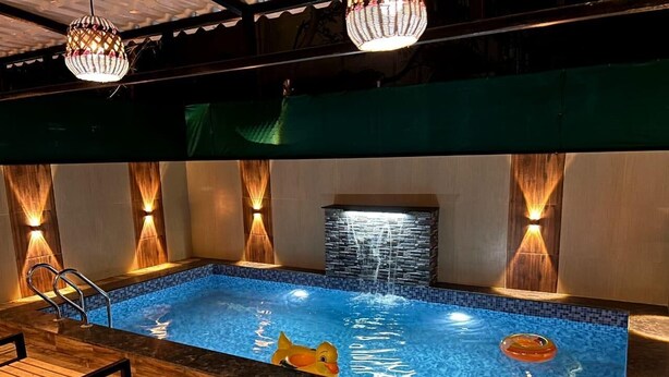 A swimming pool with a duck float, wooden deck, and wall-mounted lights. - DreamsKape Villa by CozyCub Stays in LONAVALA - 4BHK WITH POOL & JACUZZI !! (Lonavala)