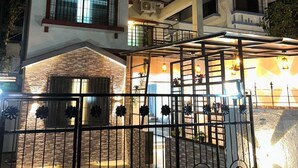 A multi-story building with a gated entrance, a balcony, and a covered area with lights. - DreamsKape Villa by CozyCub Stays in LONAVALA - 4BHK WITH POOL & JACUZZI !! (Lonavala)