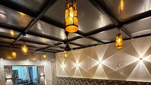 A modern lounge area with a geometric patterned wall, wooden benches, and hanging pendant lights. - DreamsKape Villa by CozyCub Stays in LONAVALA - 4BHK WITH POOL & JACUZZI !! (Lonavala)