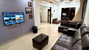 A modern living room with a flat-screen TV, a ceiling fan, a sofa, and a staircase leading to another level. - DreamsKape Villa by CozyCub Stays in LONAVALA - 4BHK WITH POOL & JACUZZI !! (Lonavala)