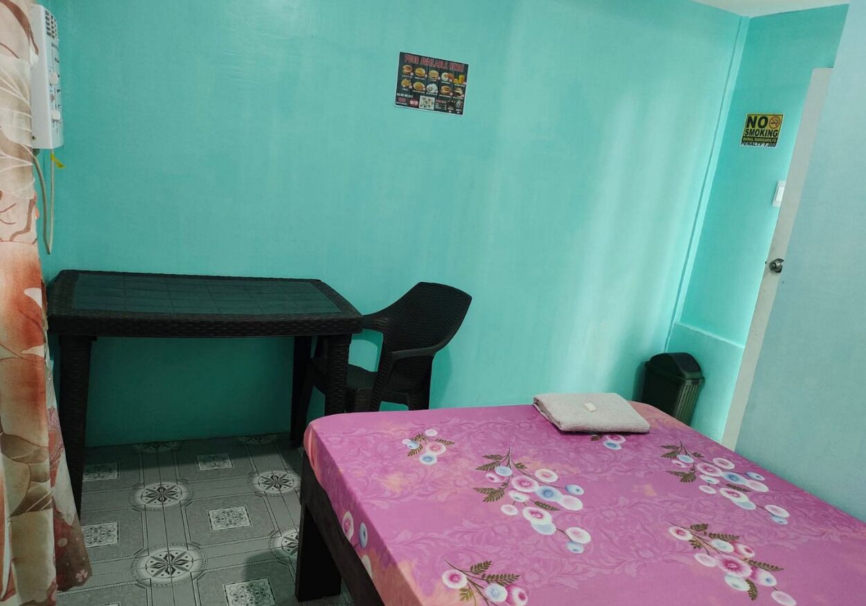Una habitación pequeña con paredes verde azulado, una colcha rosa, un escritorio y una silla.