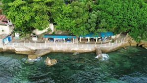 Un hotel costero con un muelle que se adentra en el agua, rodeado de abundante vegetación.