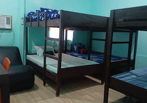 A bunk bed room with a desk and chair, a window, and a wall-mounted air conditioner.