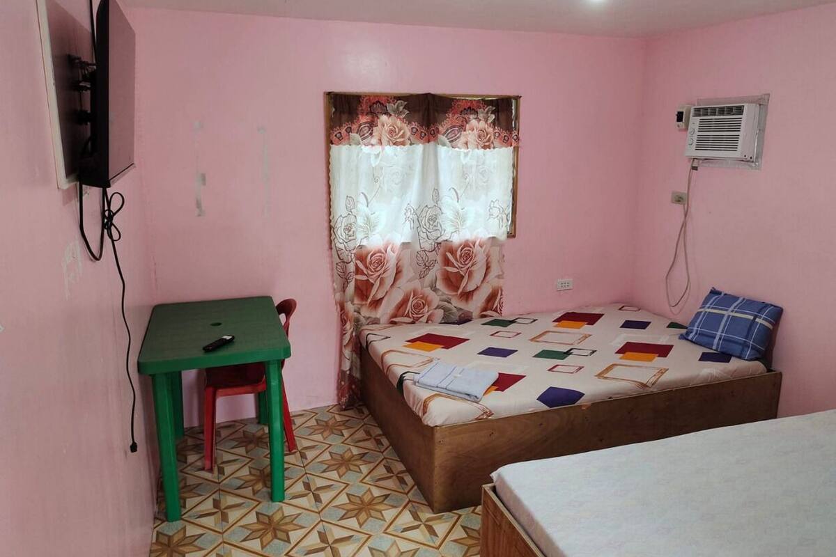 A small room with a bed, a table, a chair, a TV, and an air conditioner.