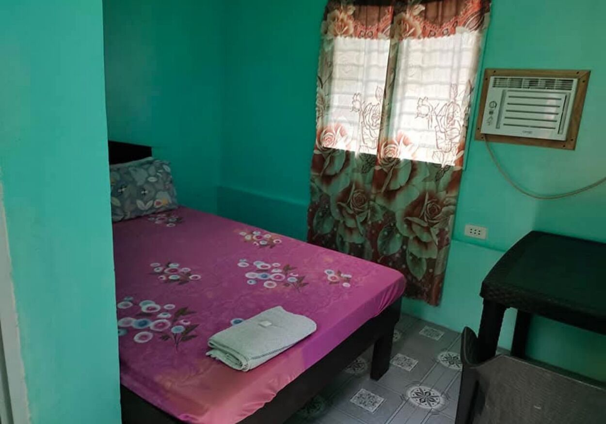 A small room with a bed, a desk, and a window with curtains.