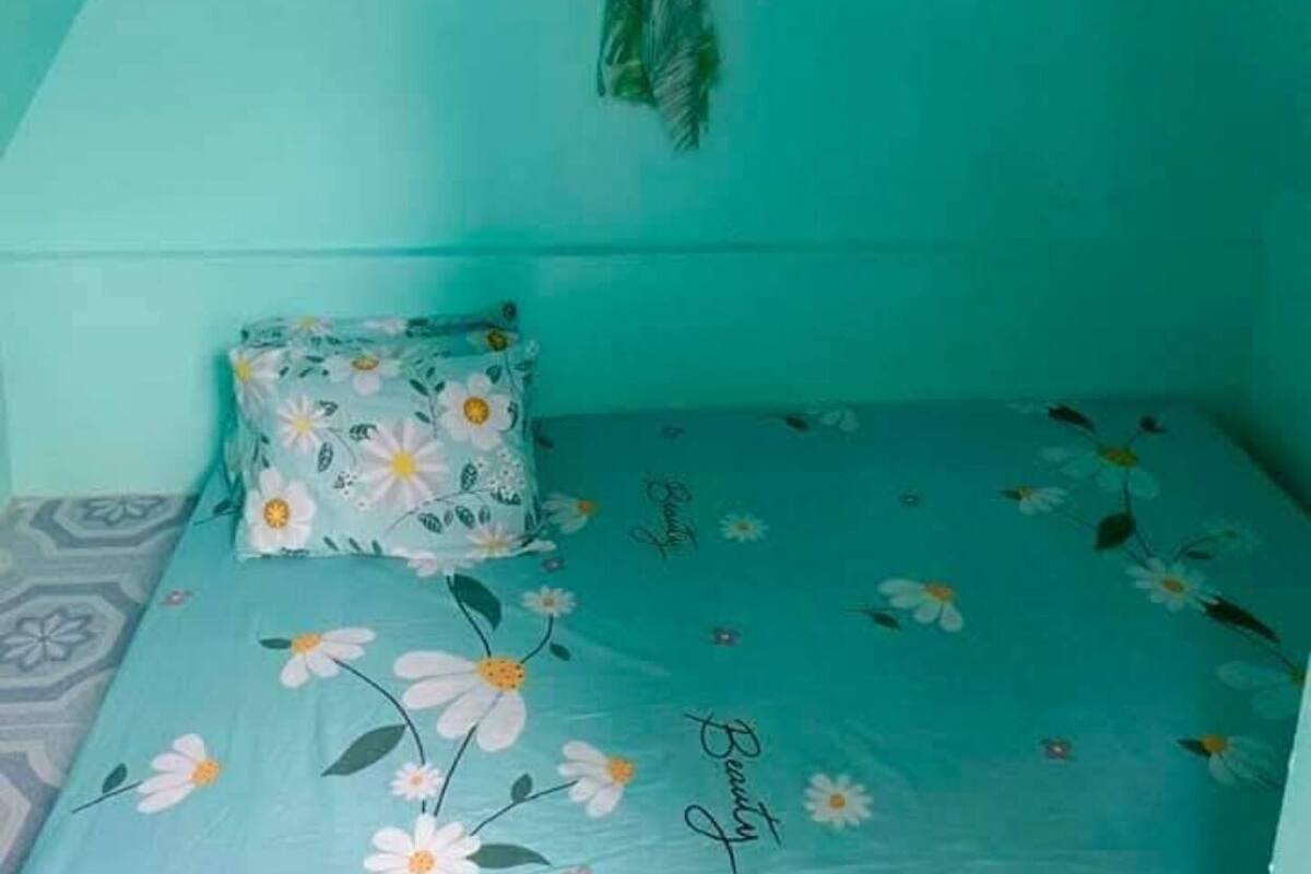 A room with a teal wall, a bed with a floral bedspread, and a matching pillow.