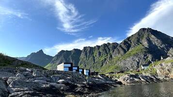 A coastal building with a rocky shoreline, a mountain backdrop, and clear skies.