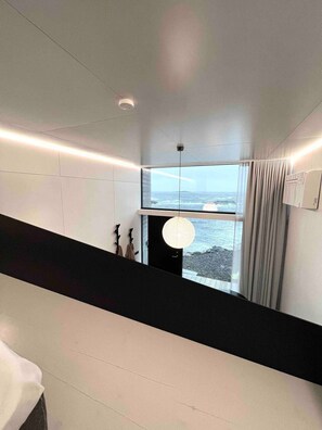 Ein modernes Interieur mit einem großen Fenster, einer Hängeleuchte und Meerblick.