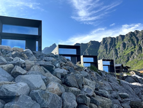 Un edificio moderno con amplias ventanas, rodeado de terreno rocoso y montañas.