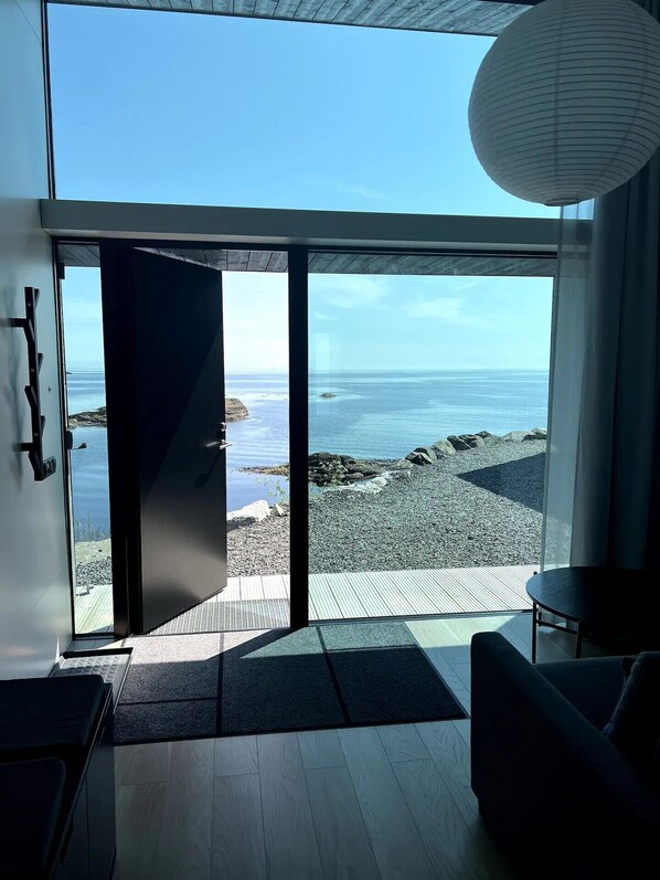 Un interior moderno con un amplio ventanal que da a una vista de la playa, piso de madera y una zona de estar sencilla.