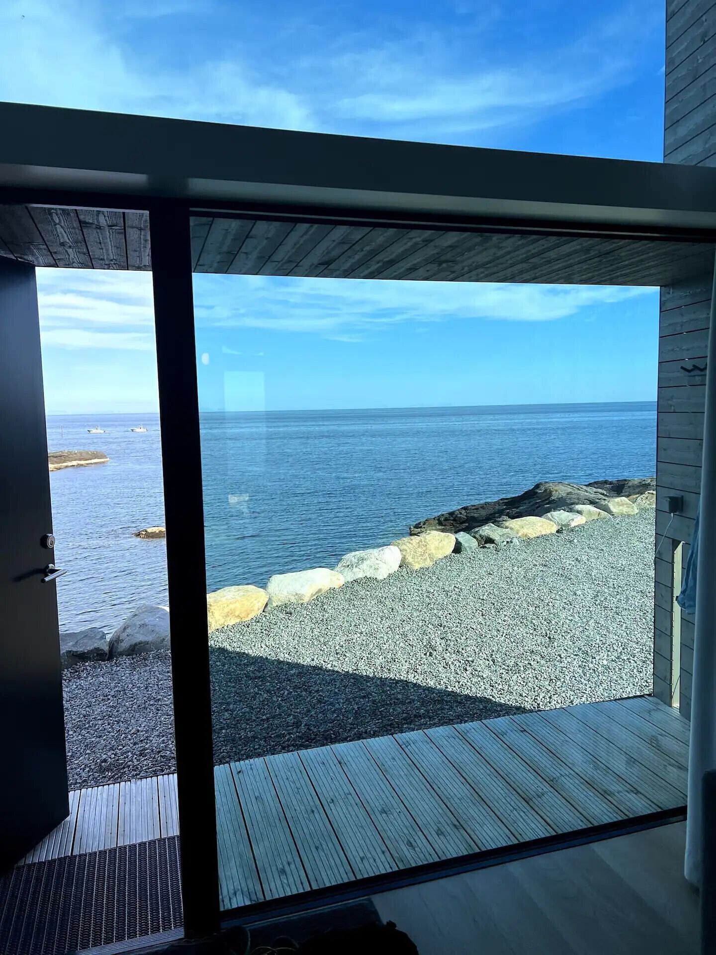 En modern inredning med en stor glasdörr som leder ut till en terrass med utsikt över stranden.