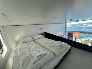 Un dormitorio moderno con una cama grande, vista al mar y una lámpara colgante.