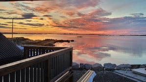 A waterfront view with a wooden deck, a small lighthouse, and calm water reflecting the sky.
