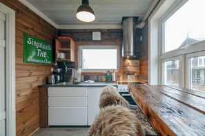 A kitchen with wooden walls, a window, and a sign reading 'Singalawatte The Iversen & Larsen.' - Arctic Lofoten Mini Retreat - Enjoy the silence! (Vestvågøy)