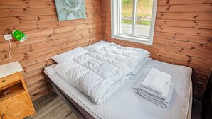 A wooden-paneled room with a bed, a window, and a wall-mounted power outlet.