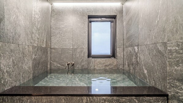 Une salle de bain moderne avec une douche à parois de verre, des murs en marbre et une fenêtre.