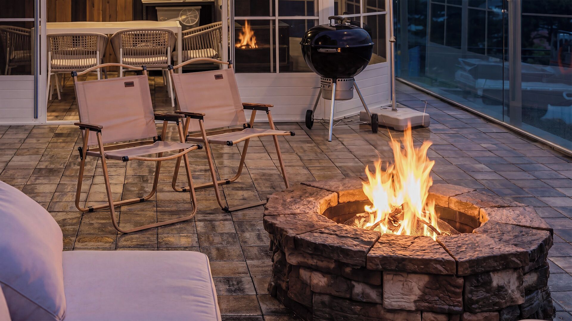 A patio with a stone fire pit, outdoor seating, and a grill.